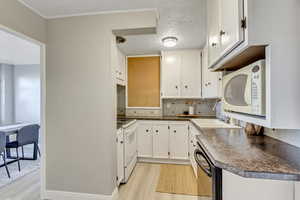 Kitchen with decorative backsplash, dark countertops, white cabinetry, a textured ceiling, and white appliances