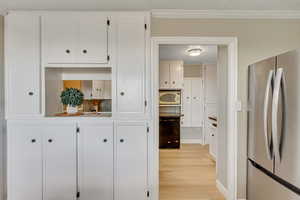 Kitchen with freestanding refrigerator, white cabinetry, light wood-style flooring, black dishwasher, and crown molding
