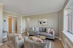 Living area with radiator heating unit, ornamental molding, and light wood finished floors