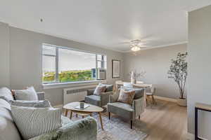 Living room featuring wood finished floors, radiator, ornamental molding, and ceiling fan