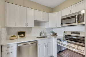 Kitchen featuring appliances with stainless steel finishes, decorative backsplash, white cabinetry, and light stone countertops