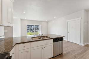 Kitchen with dark stone counters, dishwasher, light wood-type flooring, white cabinetry, and recessed lighting