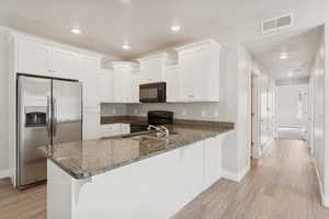 Kitchen featuring black appliances, recessed lighting, white cabinets, dark stone countertops, and light wood-type flooring