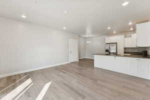 Kitchen with white cabinetry, a peninsula, light wood-style floors, a chandelier, and dark stone countertops