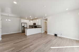 Kitchen with stainless steel refrigerator with ice dispenser, open floor plan, pendant lighting, recessed lighting, and white cabinets