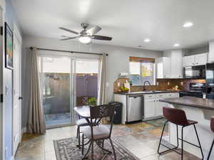 Kitchen featuring white cabinets, dark countertops, black appliances, backsplash, and a ceiling fan