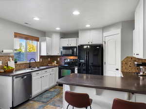 Kitchen with dark countertops, black appliances, white cabinetry, tasteful backsplash, and recessed lighting