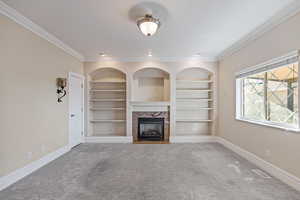 Unfurnished living room with a fireplace, carpet, built in features, and crown molding