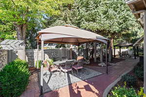 Decorative brick patio with a gazebo, a fenced backyard, water features, pine trees, and 2 outdoor dining areas
