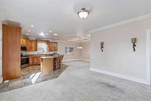 Kitchen with light carpet, recessed lighting, ornamental molding, appliances with stainless steel finishes, and a kitchen breakfast bar