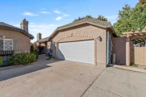 View of front facade featuring concrete driveway, stucco siding, a chimney, and a garage