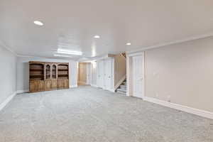 Large gathering area with fireplace, crown molding, light colored carpet, recessed lighting, stairway, and a textured ceiling