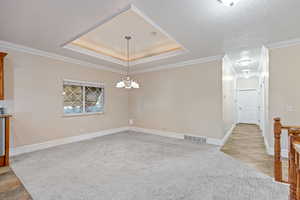 Dining room featuring a raised ceiling, crown molding, light carpet, a textured ceiling, and a chandelier