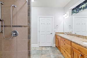 Primary bath featuring double vanity, a tile shower, and light tile patterned floors