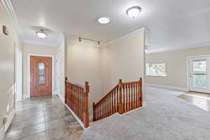 Foyer entrance featuring ornamental molding, a textured ceiling, light colored carpet, and light tile patterned flooring