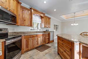 Kitchen with ornamental molding, appliances with stainless steel finishes, cherry cabinets, a raised ceiling, and light stone countertops