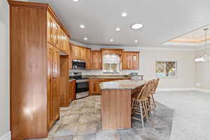 Kitchen with light stone counters, appliances with stainless steel finishes, cherry cabinetry, a kitchen island, and crown molding
