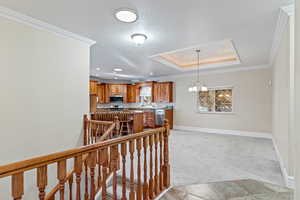 Hall with an upstairs landing, a raised ceiling, light colored carpet, ornamental molding, and a textured ceiling