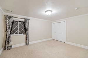 Unfurnished bedroom featuring a textured ceiling, carpet flooring, a closet, and ornamental molding