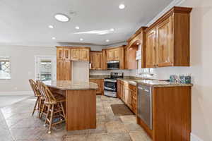 Kitchen with light granite counters, cherry cabinetry, a kitchen bar, appliances with stainless steel finishes, and ornamental molding
