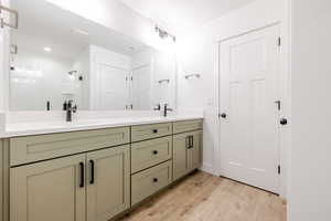 Full bathroom with double vanity, light wood-style floors, and a stall shower