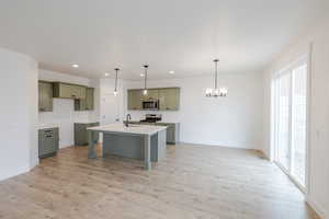 Kitchen with a breakfast bar, hanging lights, stainless steel appliances, light wood finished floors, and an island with sink