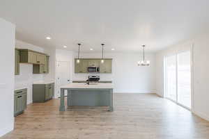 Kitchen featuring green cabinets, a kitchen island with sink, light wood-type flooring, a kitchen bar, and hanging lights