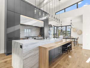 Kitchen featuring decorative light fixtures, gray cabinets, modern cabinets, light wood-type flooring, and a towering ceiling