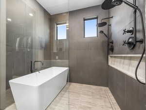 Bathroom with a walk in shower, a soaking tub, tile walls, and light tile patterned floors