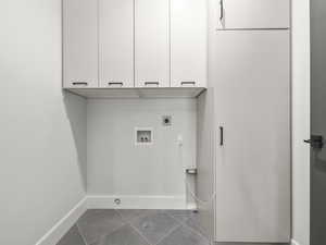 Washroom featuring dark tile patterned flooring, hookup for a washing machine, hookup for an electric dryer, and cabinet space