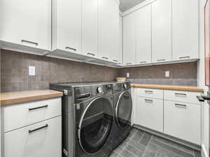 Laundry area featuring dark tile patterned flooring, washing machine and dryer, and cabinet space