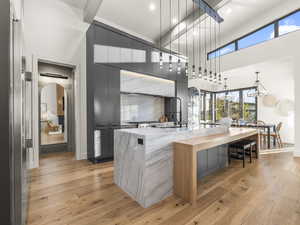 Kitchen with gray cabinets, hanging light fixtures, light wood-style flooring, a kitchen bar, and light stone countertops
