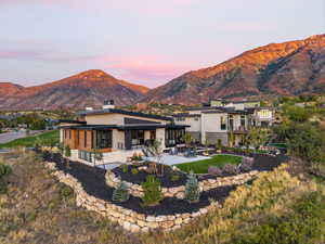 Back of property at dusk featuring a patio area, stone siding, a mountain view, and stucco siding