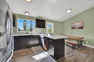 Kitchen featuring a peninsula, stainless steel appliances, dark wood-style floors, lofted ceiling, and dark brown cabinets