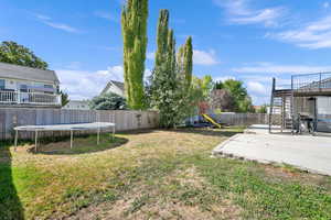 Fenced backyard with a trampoline, a patio area, a playground, and stairway