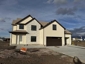 View of front facade with stone siding, a shingled roof, driveway, an attached garage, and stucco siding