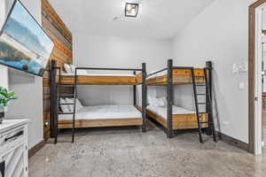 Bedroom with a textured ceiling, concrete floors, and wood walls