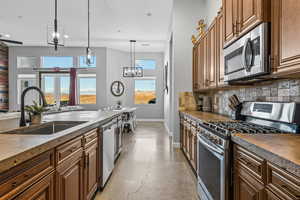 Kitchen with appliances with stainless steel finishes, brown cabinets, finished concrete flooring, pendant lighting, and backsplash
