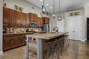 Kitchen featuring tasteful backsplash, a center island with sink, a breakfast bar area, stainless steel appliances, and hanging light fixtures