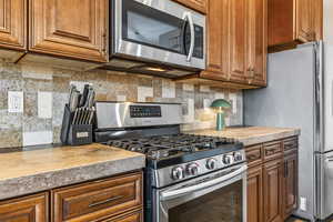 Kitchen with stainless steel appliances, brown cabinets, decorative backsplash, and light countertops