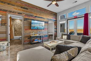 Living room featuring wooden walls, ceiling fan, french doors, and concrete flooring