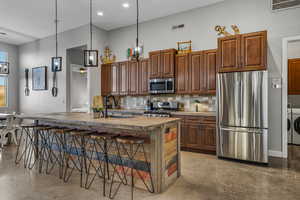Kitchen with stainless steel appliances, a breakfast bar area, concrete flooring, backsplash, and recessed lighting