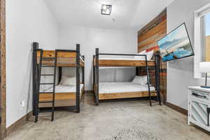 Bedroom featuring a textured ceiling, concrete flooring, and wooden walls