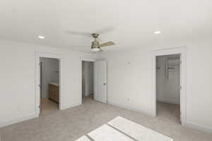 Unfurnished bedroom featuring light colored carpet, recessed lighting, a walk in closet, ensuite bath, and ceiling fan