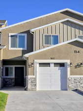 View of front facade featuring stone siding, stucco siding, an attached garage, and driveway
