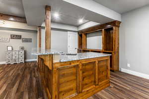 Kitchen featuring light stone countertops, dark wood-style floors, brown cabinets, a breakfast bar area, and a center island