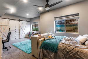 Bedroom featuring carpet floors, a barn door, a textured ceiling, a desk, and ceiling fan