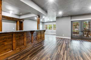 Bar with light stone countertops, dark wood-style flooring, and french doors