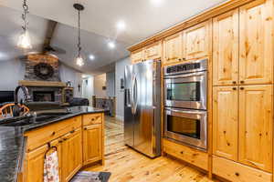 Kitchen with stainless steel appliances, light wood-style floors, hanging light fixtures, open floor plan, and dark stone counters