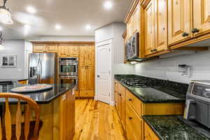 Kitchen with light wood finished floors, pendant lighting, dark stone counters, appliances with stainless steel finishes, and recessed lighting